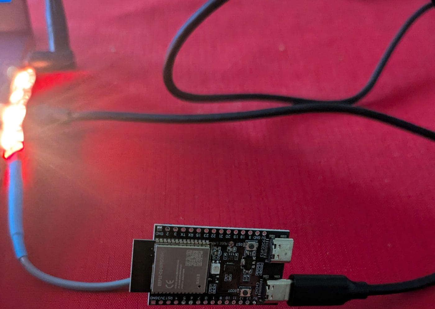 ESP32-C6 board with its WS2812B strip glowing red and orange during a beacon flood