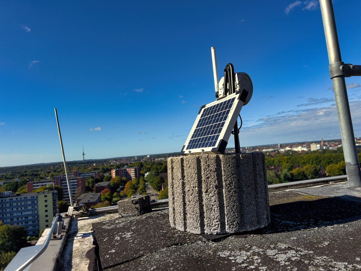 A solar panel and antenna mast mounted on a concrete plinth on a rooftop, part of a RAK4631-based mesh repeater running entirely off-grid on solar power